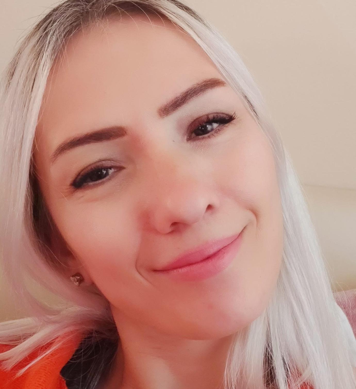 Close-up casual selfie of a blonde woman smiling warmly at the camera.